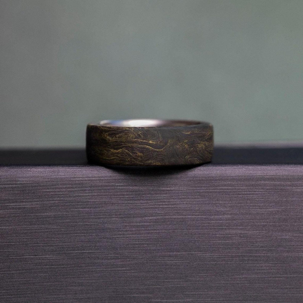 Carbon fiber ring with gold flake detail, dark textured surface close-up