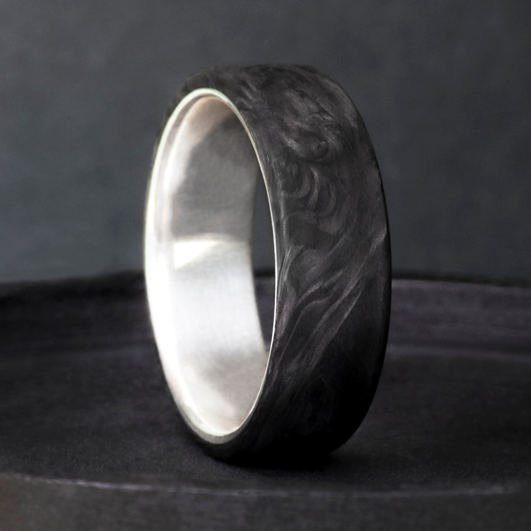 Mens wedding band in forged carbon fiber with swirling matte texture and sterling silver interior