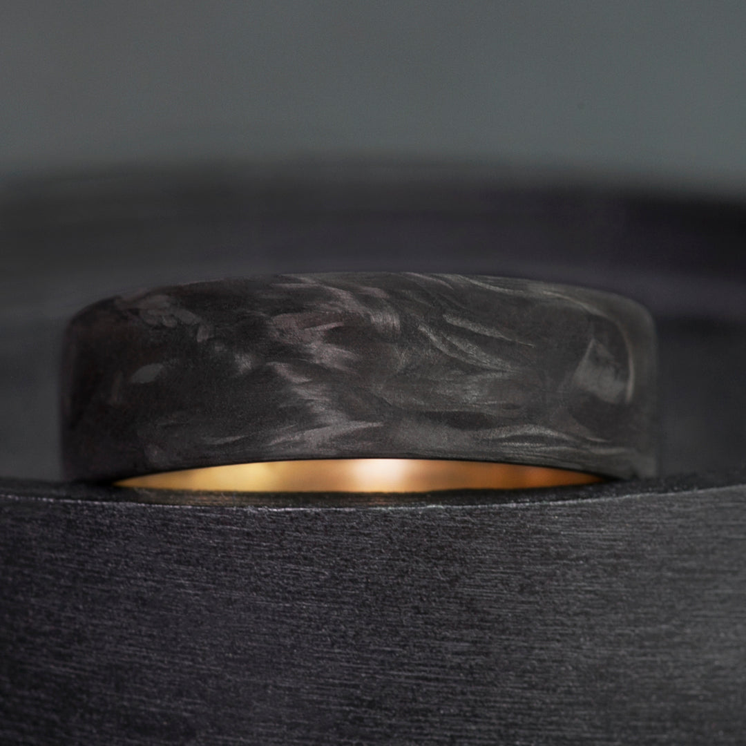 Mens wedding band in forged carbon fiber with swirling matte texture and polished brass sleeve