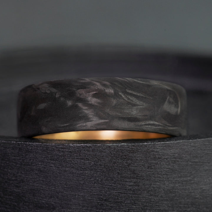 Mens wedding band in forged carbon fiber with swirling matte texture and polished brass sleeve