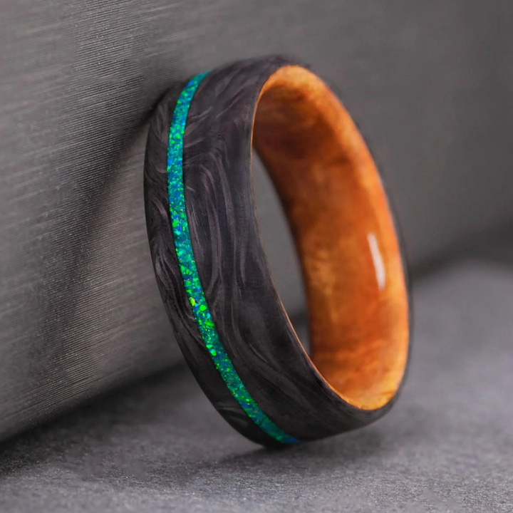 Opal inlay ring in dark carbon fiber, with the blue-green opal shifting color in the light