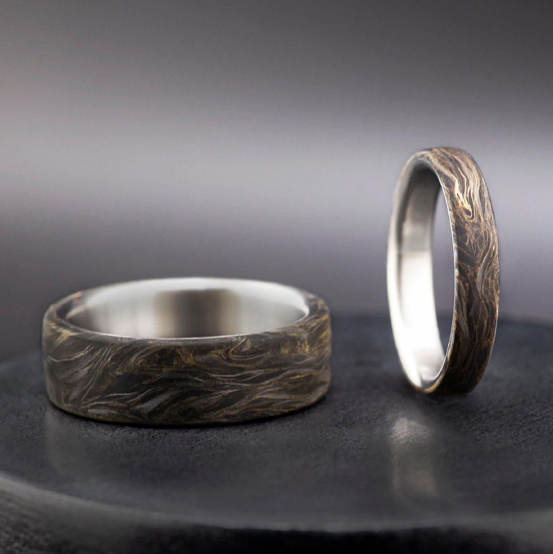 Handcrafted titanium and carbon fiber wedding band with swirling gold leaf accents