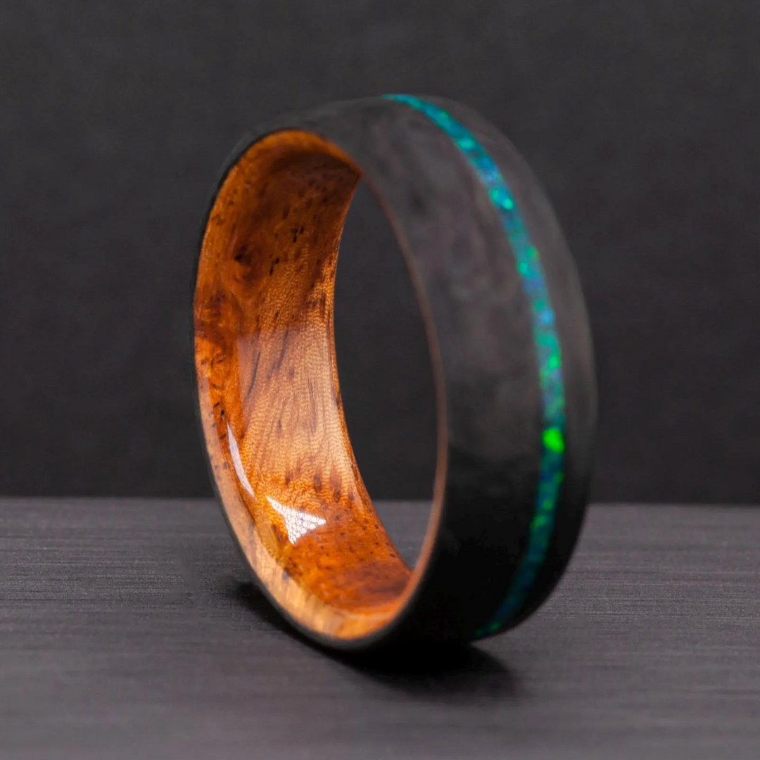 The Aurora carbon fiber wedding band standing upright on a dark background, opal inlay and wood interior visible