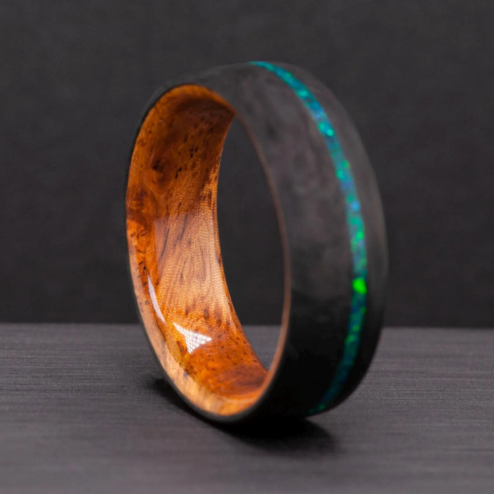 The Aurora carbon fiber wedding band standing upright on a dark background, opal inlay and wood interior visible